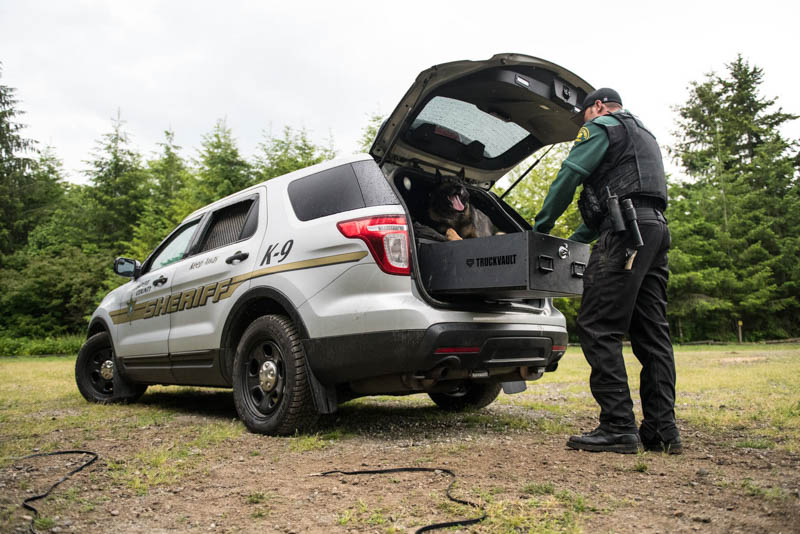 A silver, police department Ford Explorer with a dog and an officer opening a TruckVault.