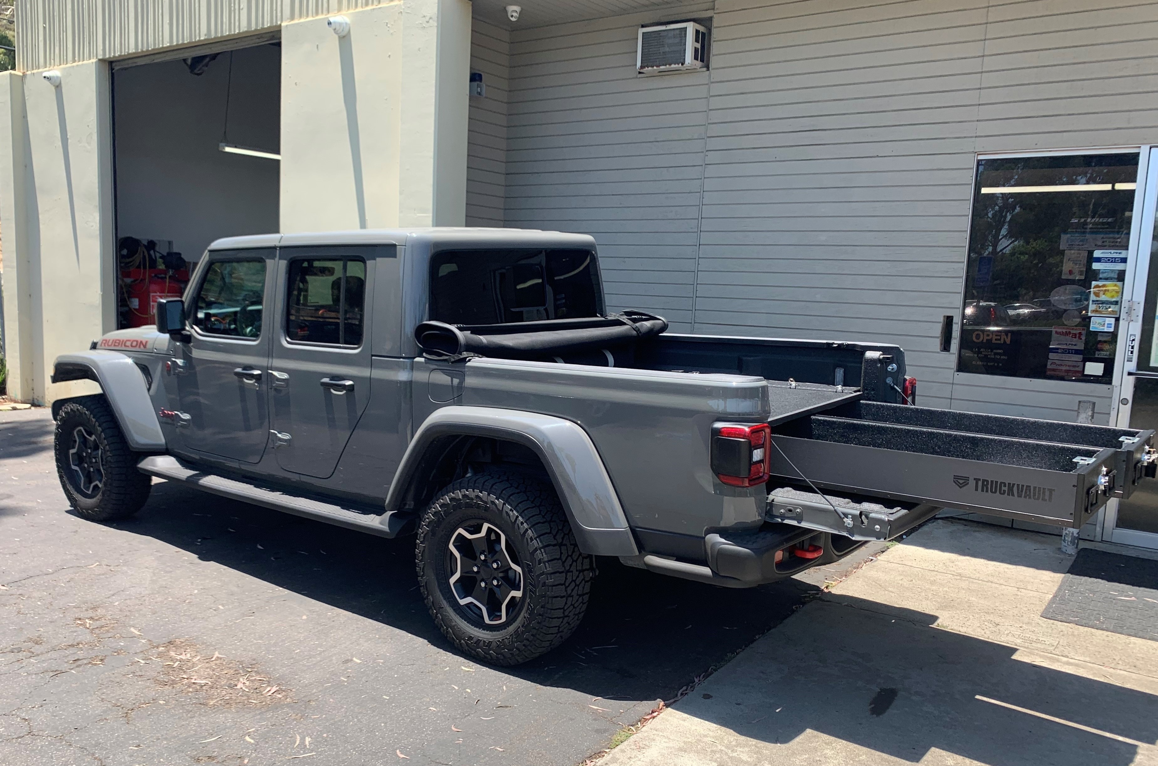 A silver Jeep Gladiator with an All-Weather TruckVault secure storage systemparked on a street.
