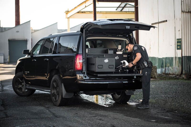 A black Chevy Tahoe with a police officer setting up his drone on his TruckVault pullout table.