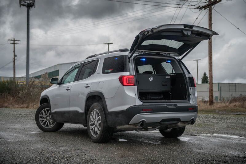 A silver GMC Acadia on a gravel road with a TruckVault in the cargo space for secure storage.