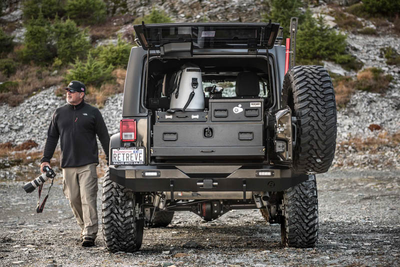 A silver Jeep Wrangler Unlimited with a custom TruckVault and a man carrying a camera.