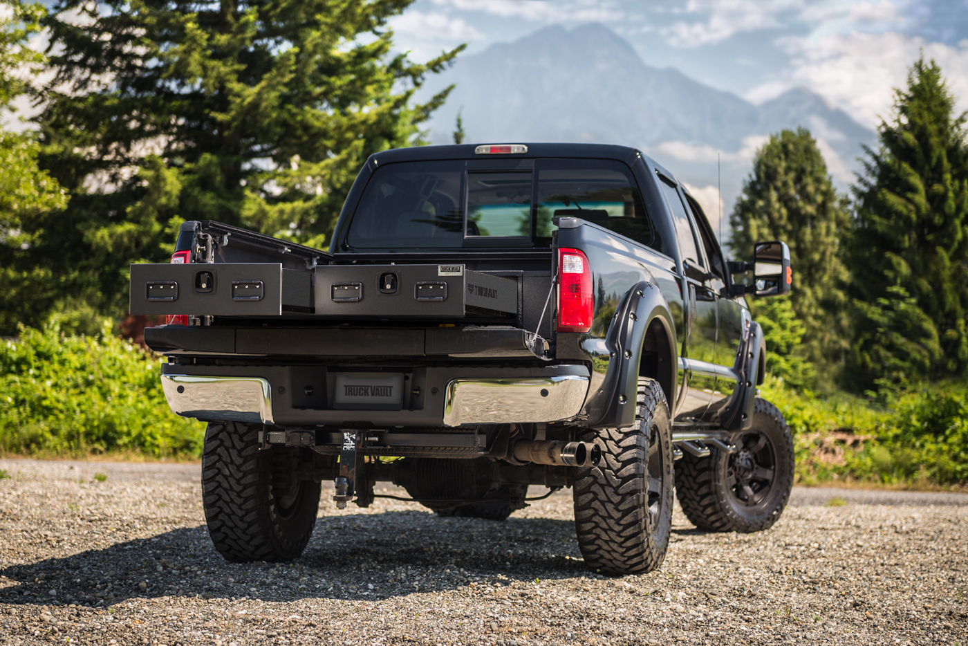 A black Ford F-350 on a gravel road with an open TruckVault.