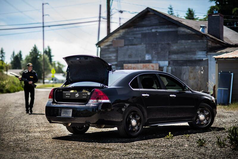 A law enforcement offer walking towards a black Chevy Impala with a TruckVault in the trunk for secure storage.