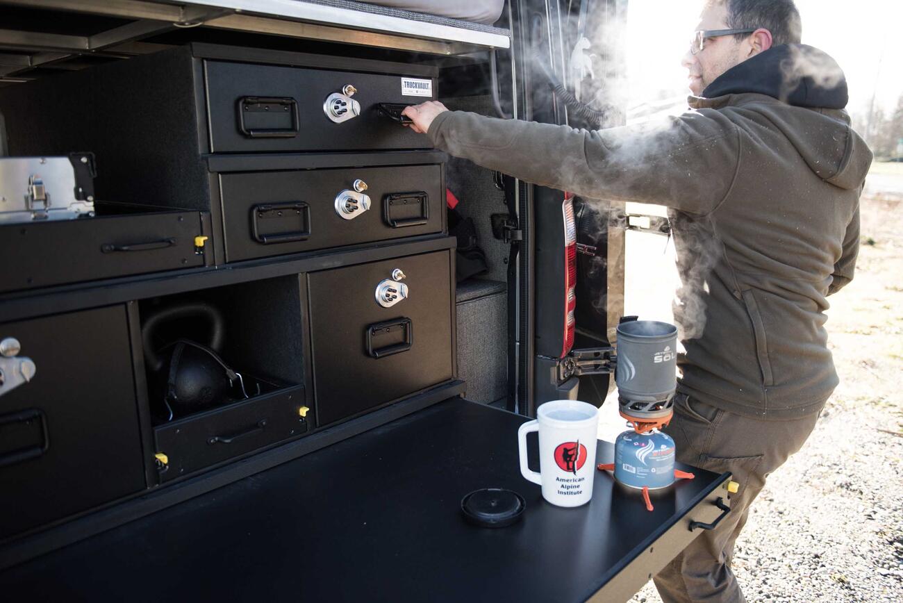 A man opening a TruckVault secure storage system while he brews coffee on a TruckVault extension table.