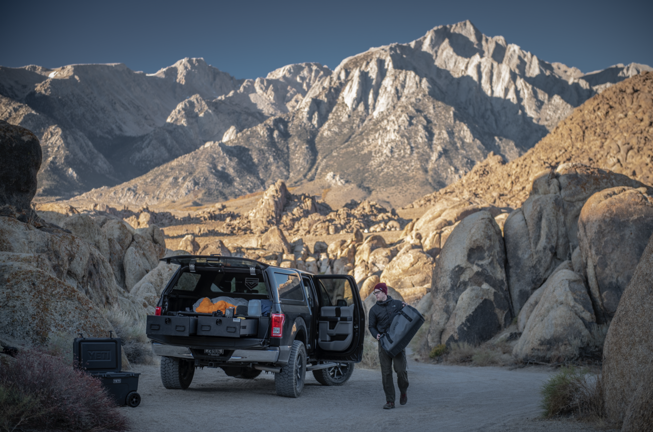outdoorsman paking gear into drawer of TruckVault secure truck bed storage system for covered pickup trucks with mountains in background