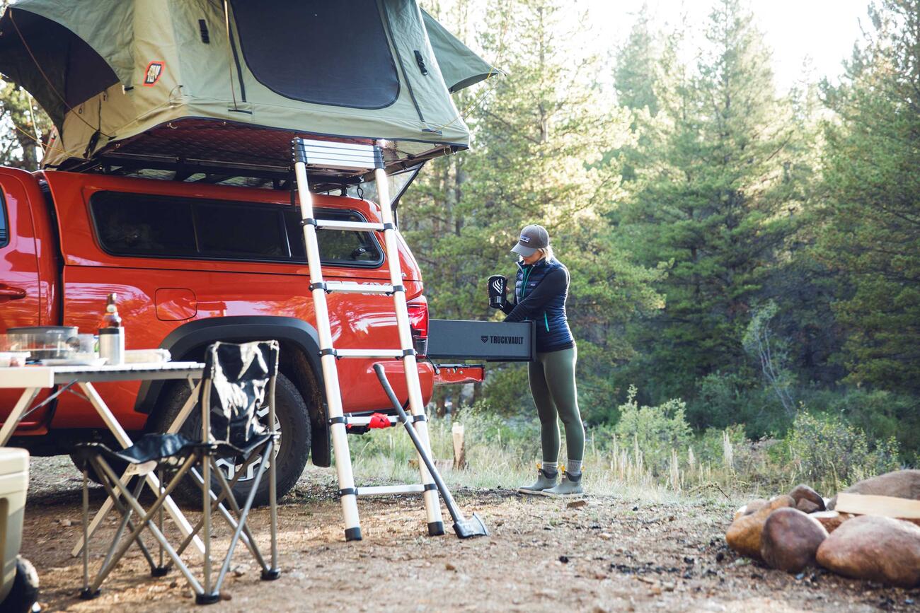 A woman taking gear out a TruckVault that is in the bed of a red truck.