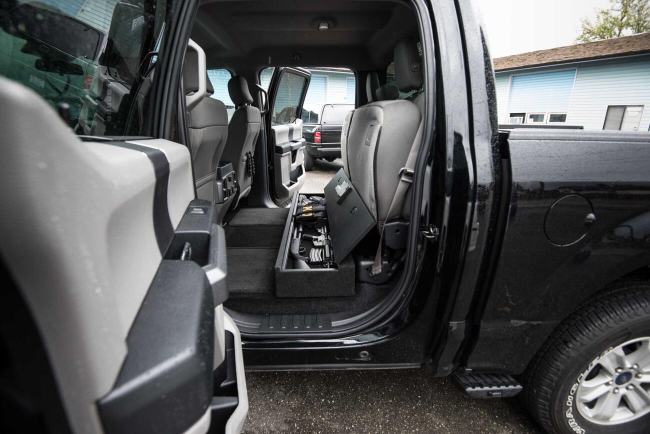 PickUpSeries_InteriorCabLine_SeatVault_Ford_F150_McInturf-6.jpg A black Ford F150 with an open SeatVault with guns and other police gear.