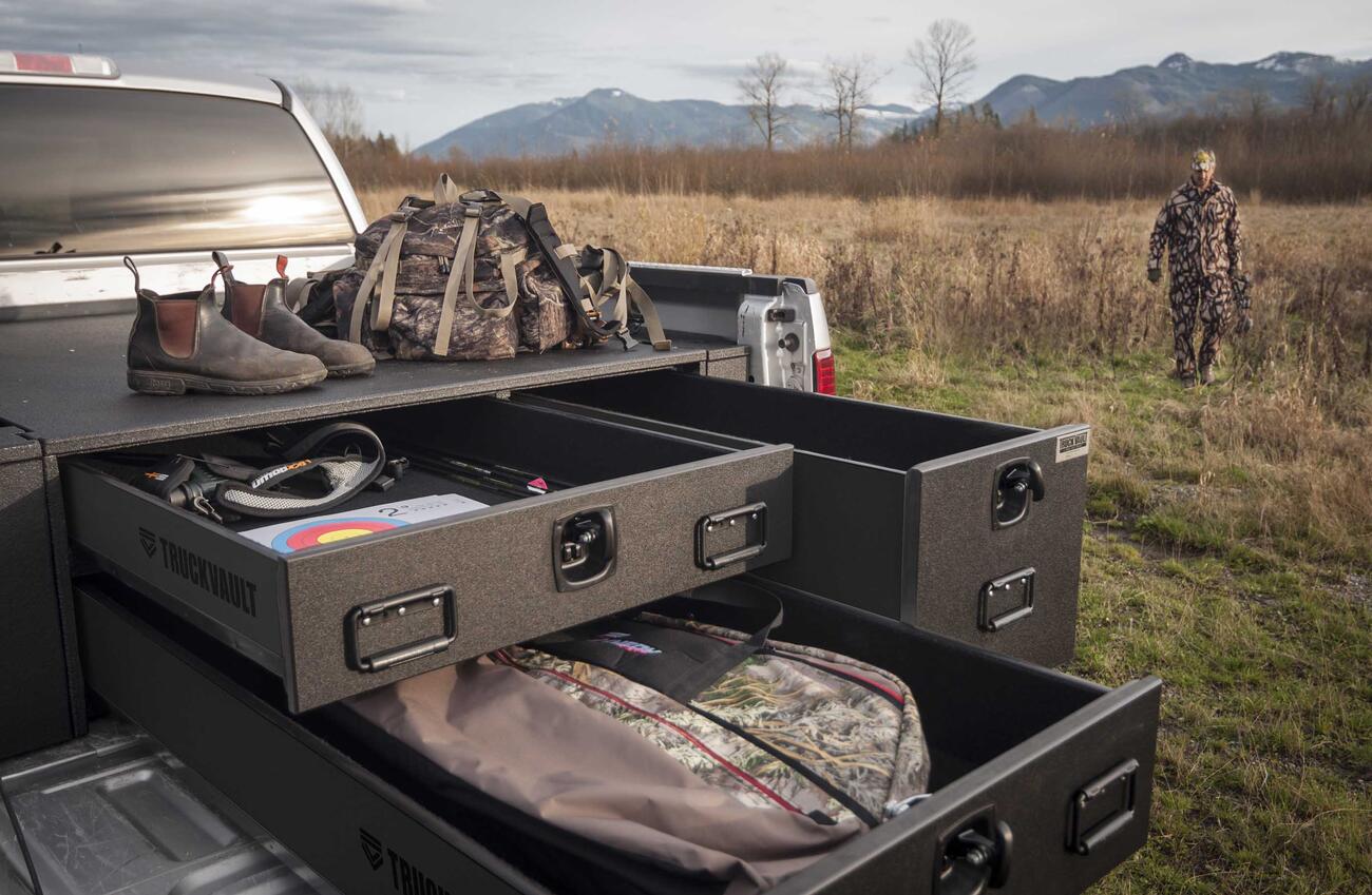 PickupSeries_All-WeatherLine_BowVault_2010_Ford_F150_ElkHunting1.jpg A man walking towards his Ford F-150 TruckVault with his bow hunting gear as well as boots and other equipment.