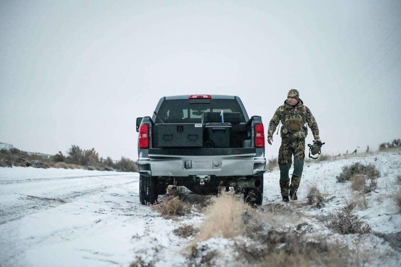 A man in camouflage with a bow walking away from a parked Chevy Silverado with a Half Width TruckVault in the bed.