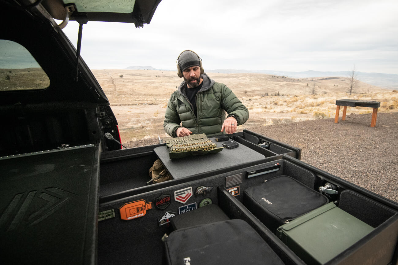 A man loading his magazines with ammunition on top of his TruckVault standing in front of a shooting range.