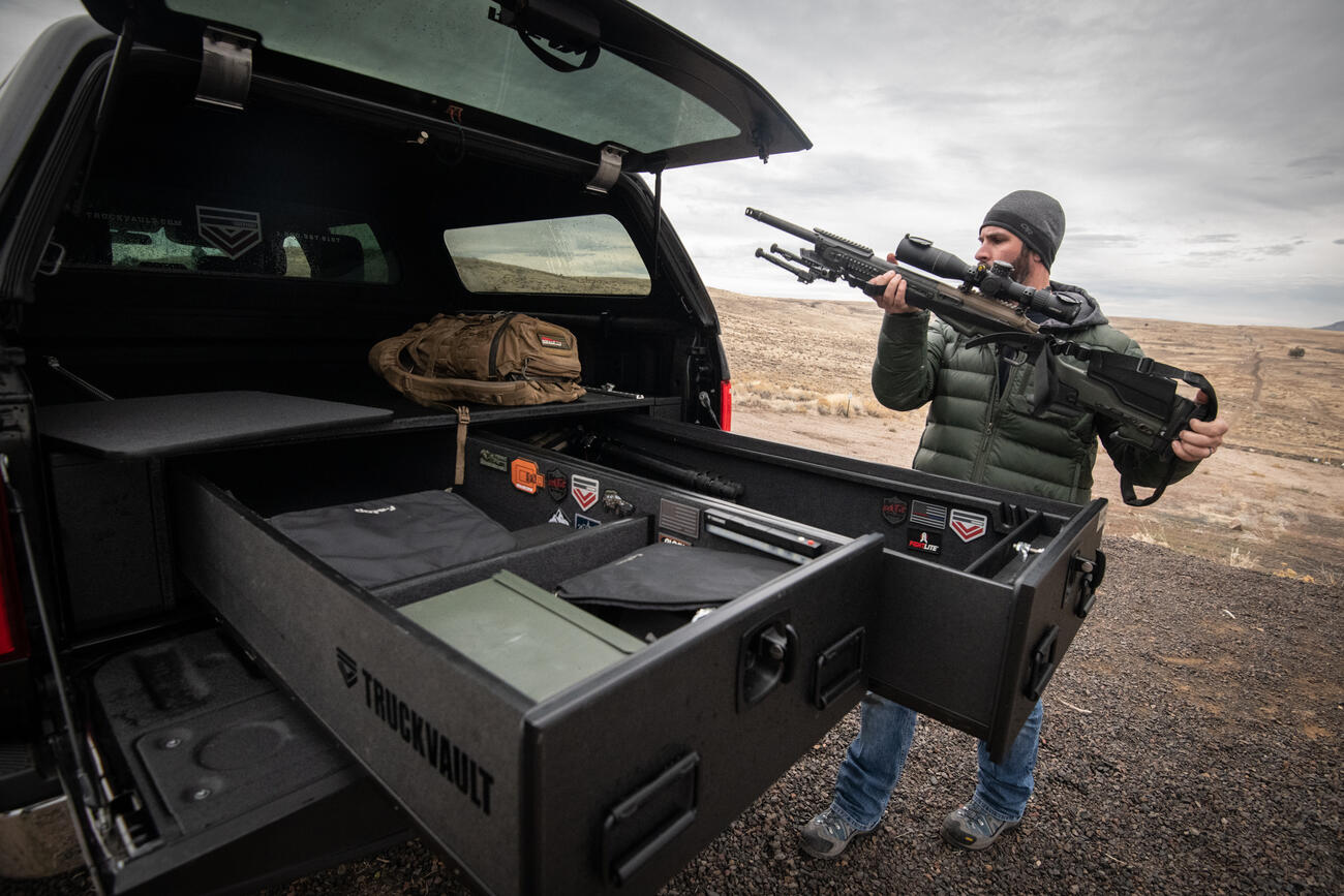 A man placing his rifle into his TruckVault which is in the back of his Ford F-150.