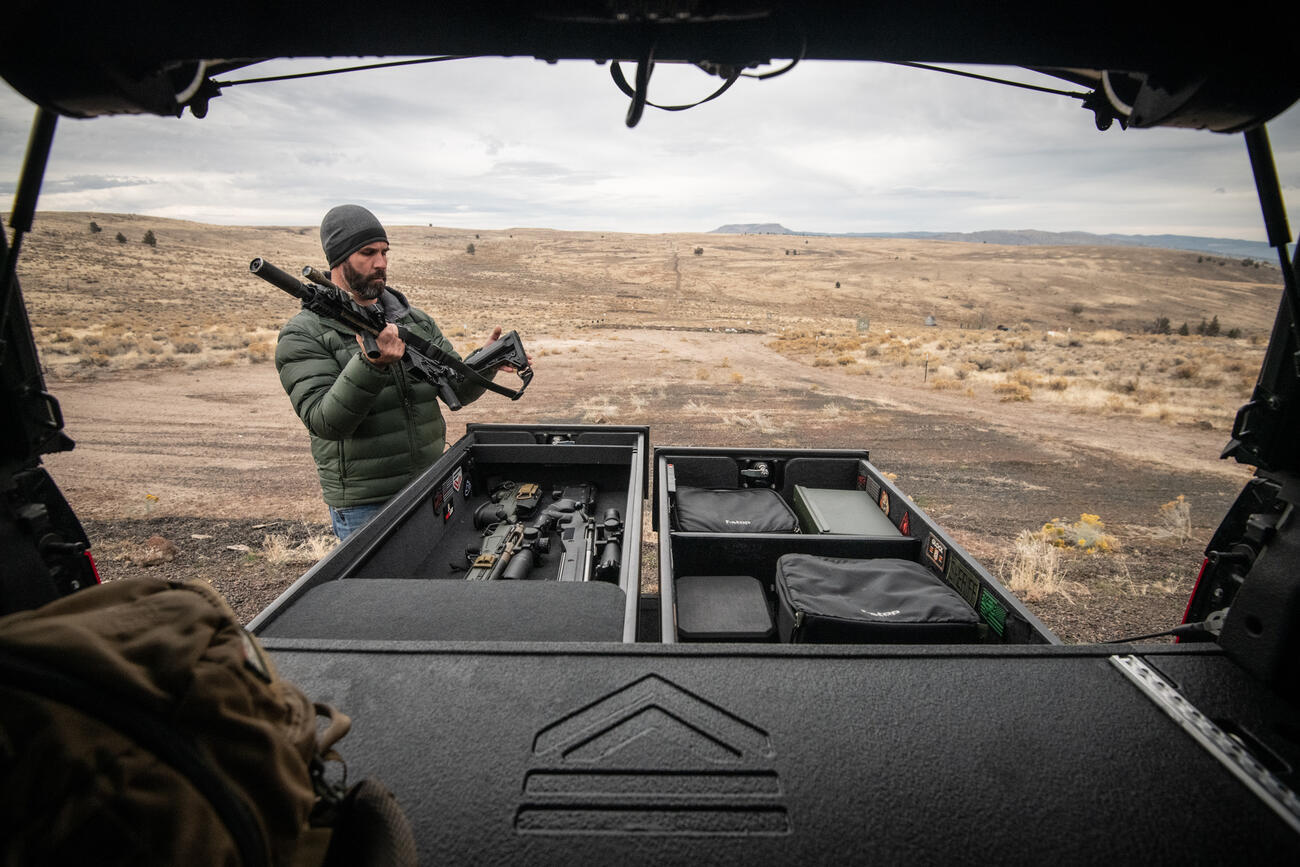 A man folding the stock of his rifle while standing next to a TruckVault in front of a rifle range.