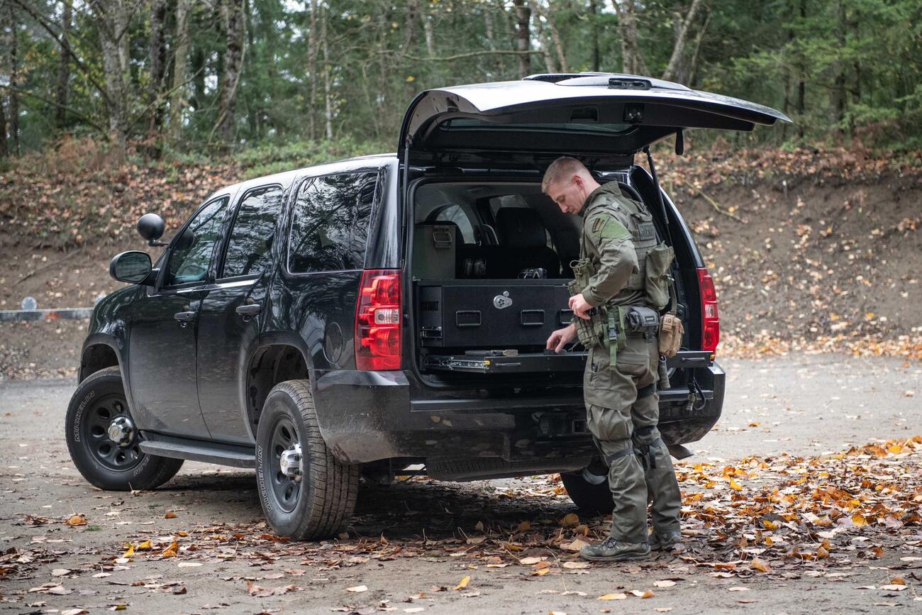 A man loads his magazine on a heavy duty pull out table in the back of a Chevy Tahoe.