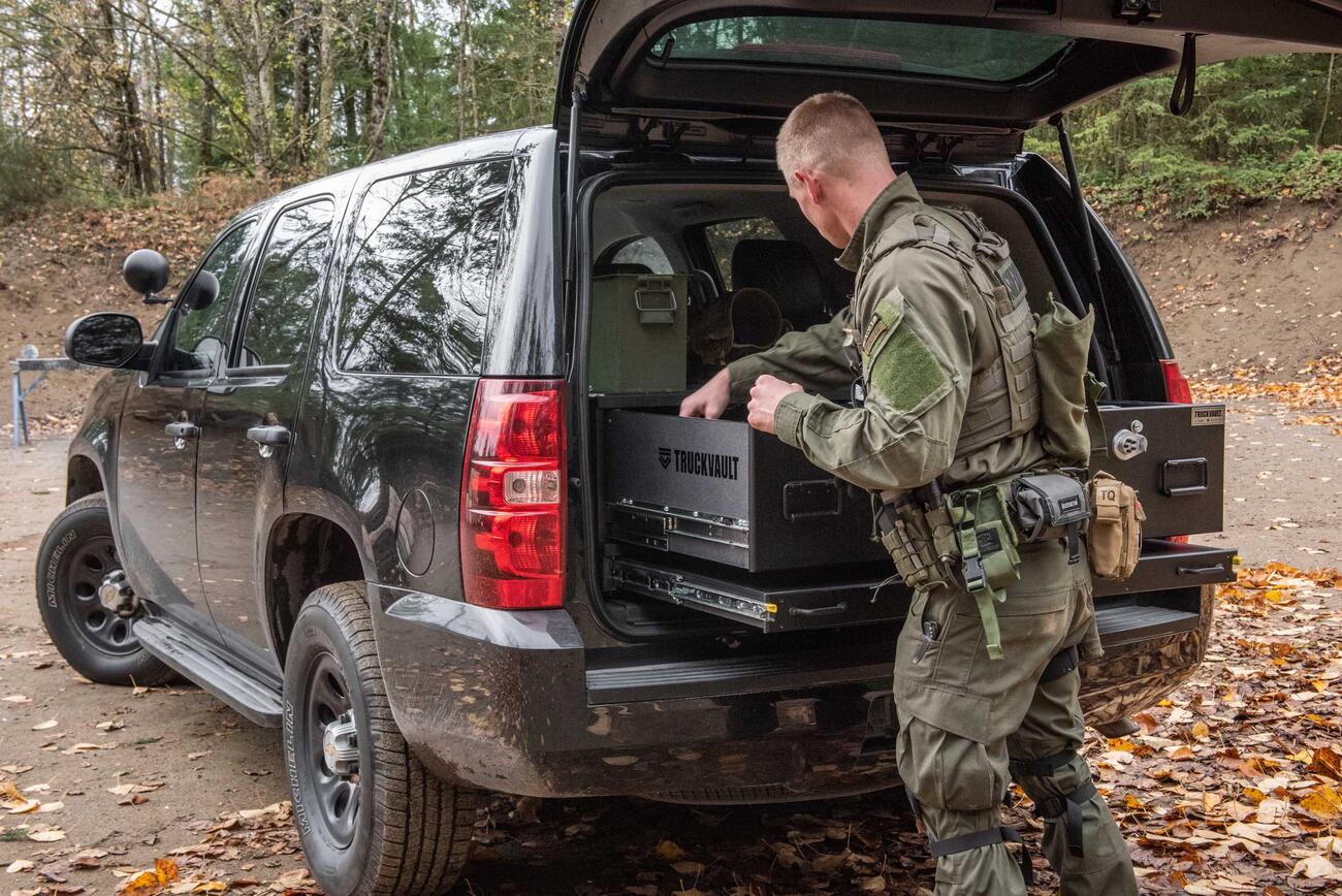 A man wearing tactical clothing grabbing equipment out of a TruckVault inside of a black Chevy Tahoe.