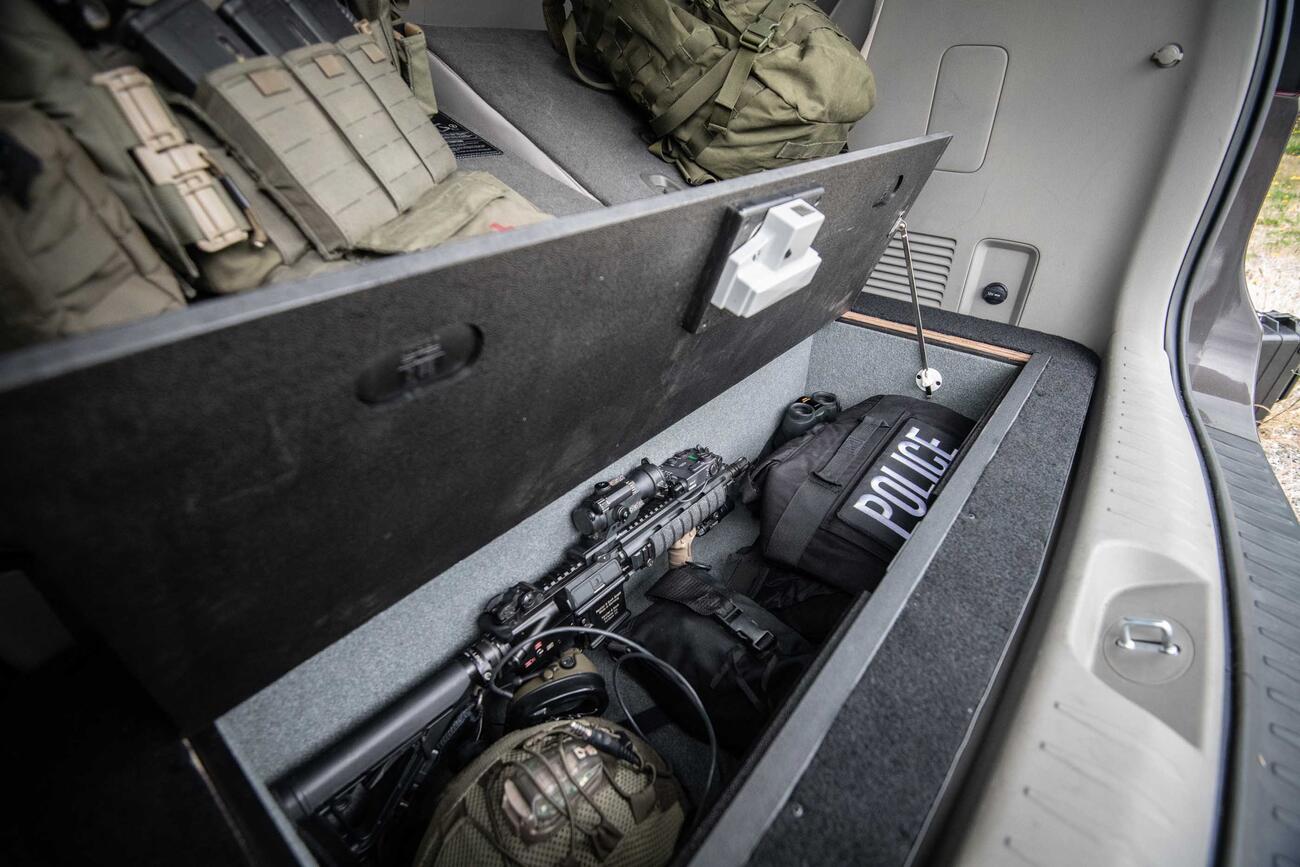 Law Enforcement An oper Kia Sedona floorvault filled with a gun and police gear, next to two backpacks.