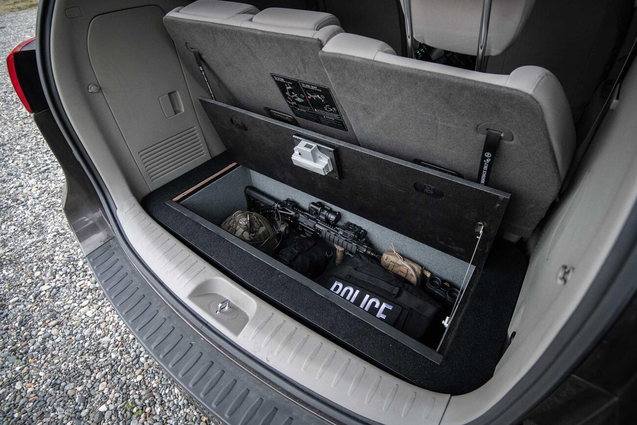 An open Kia Sedona FloorVault filled with a gun and police gear.