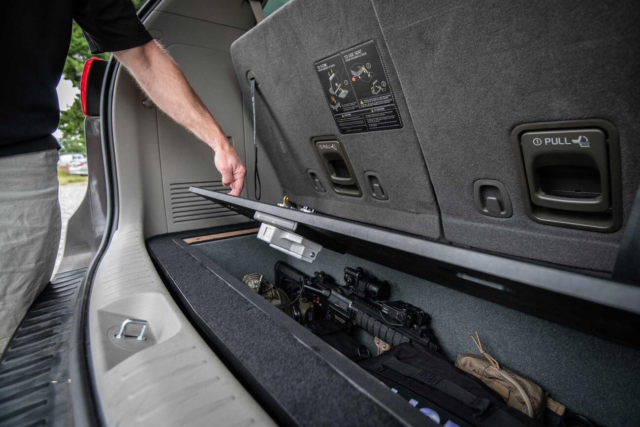 A man opening a Kia Sedona FloorVault filled with a gun and other police gear.