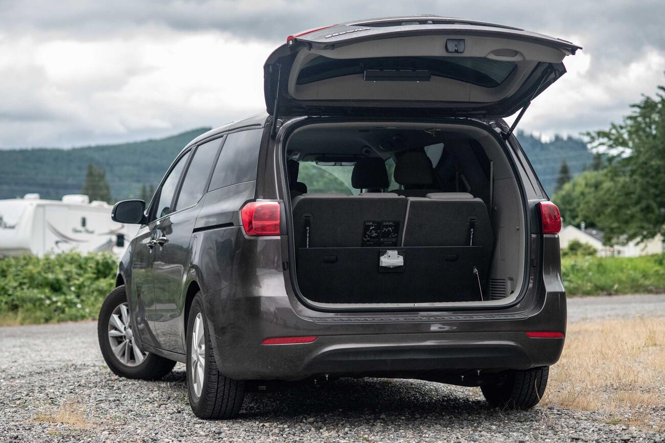 The back side of a black KiaSedona with an open trunk and an open FloorVault.