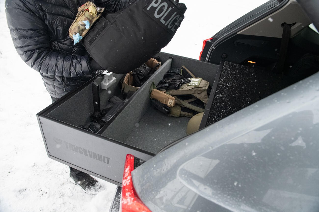 A police officer grabbing a vest out of a TruckVault, which is in a VW Atlas, which is parked in the snow.