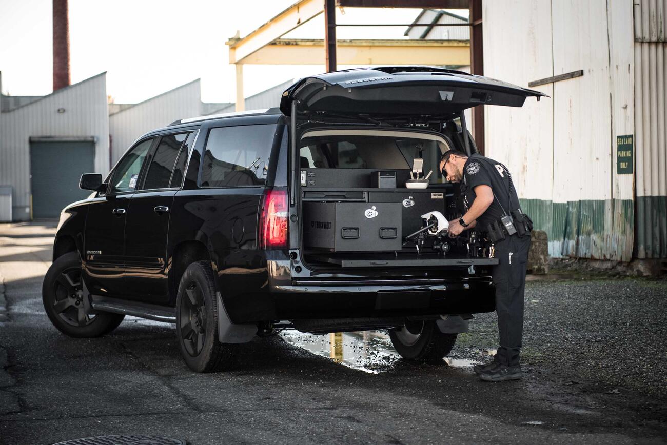 A police officer working on his drone on a pull-out table attached to his black Chevy Suburban.