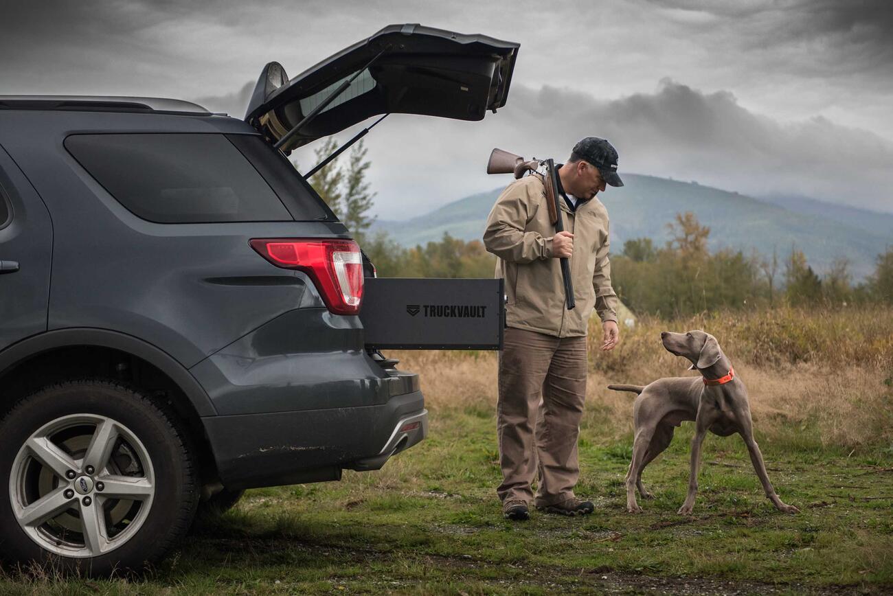 Hunter with gun and dog standing next to SUV with open hatch and TruckVault secure storage drawer extended