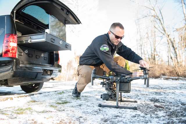 A man crouching down next to his truck, setting up his drone so he could take flight.