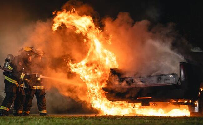 Two firemen spray water at a burning pickup truck with a TruckVault drawer system installed