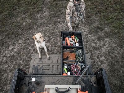 hunter opening TruckVault secure truck bed storage system in back of Ford F-150 with hunting dog nearby