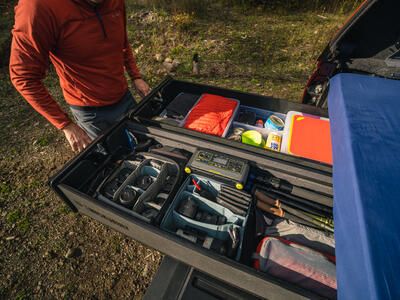 hiker opens drawers of TruckVault secure truck bed storage revealing hiking and photography gear