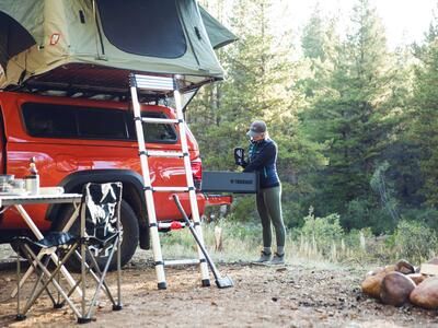 A woman taking gear out a TruckVault that is in the bed of a red truck.