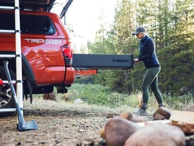 A red truck with a roof tent and a TruckVault. The TruckVault is being opened by a woman.