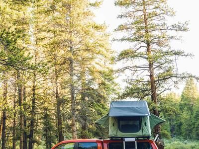 A green tent on top of a red Toyota Tacoma. There is an open TruckVault in the bed of the bed.