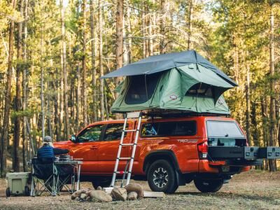 A green tent on top of a red truck. There is an open TruckVault in the back of the truck.