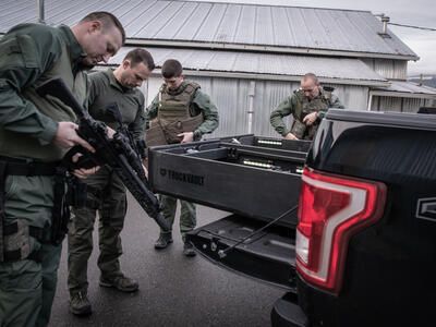 A SWAT team of four checking out their weapons while standing around an all weather TruckVault for a Ford F-150.