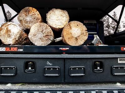 A TruckVault secure storage system in the back of a Toyota Tacoma with logs on top of the system.