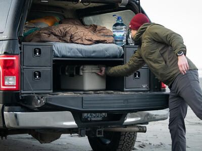 Man pulls box from storage underneath sleeping platform in TruckVault Base Camp 4