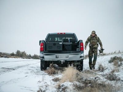 A man in camouflage with a bow walking away from a parked Chevy Silverado with a Half Width TruckVault in the bed.