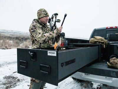 A man in camouflage grabbing his compound bow out of a Half Width TruckVault in the snow.