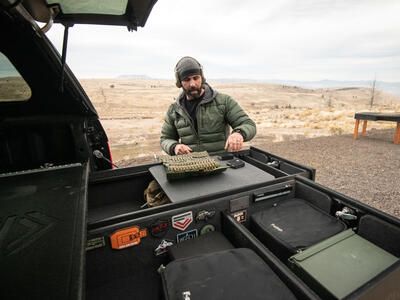 A man loading his magazines with ammunition on top of his TruckVault standing in front of a shooting range.