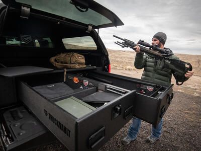 A man placing his rifle into his TruckVault which is in the back of his Ford F-150.