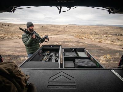 A man folding the stock of his rifle while standing next to a TruckVault in front of a rifle range.