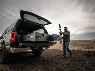 A man grabbing his assault rifle out of the back of his TruckVault in a Ford F-150.