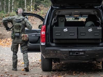 A man with a gun standing next to a black Chevy Tahoe that has a TruckVault in it.