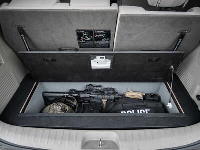 An open Kia Sedona FloorVault filled with a gun and police gear.