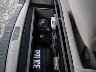 An open Kia Sedona FloorVault filled with a gun and police gear.