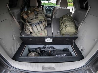 A Kia Sedona FloorVault filled with a gun and police gear. Next to two police backpacks.