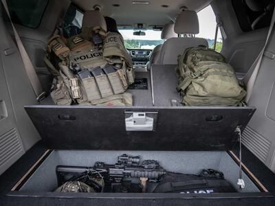 A Kia Sedona with an open SeatVualt containg a gun and police gear. Next to two police backpacks.