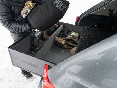 A police officer grabbing a vest out of a TruckVault, which is in a VW Atlas, which is parked in the snow.