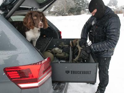 A police officer grabbing gear out of a TruckVault, with a dog sitting on top of the TruckVault.