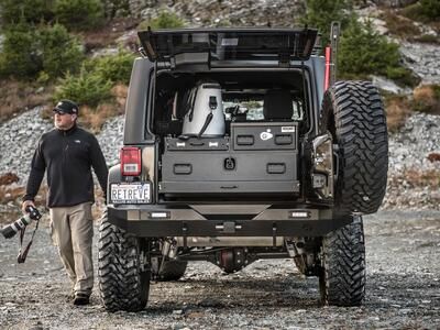 A man with a camera walking next to a 2013 Jeep Wranger with a TruckVault in the cargo space.